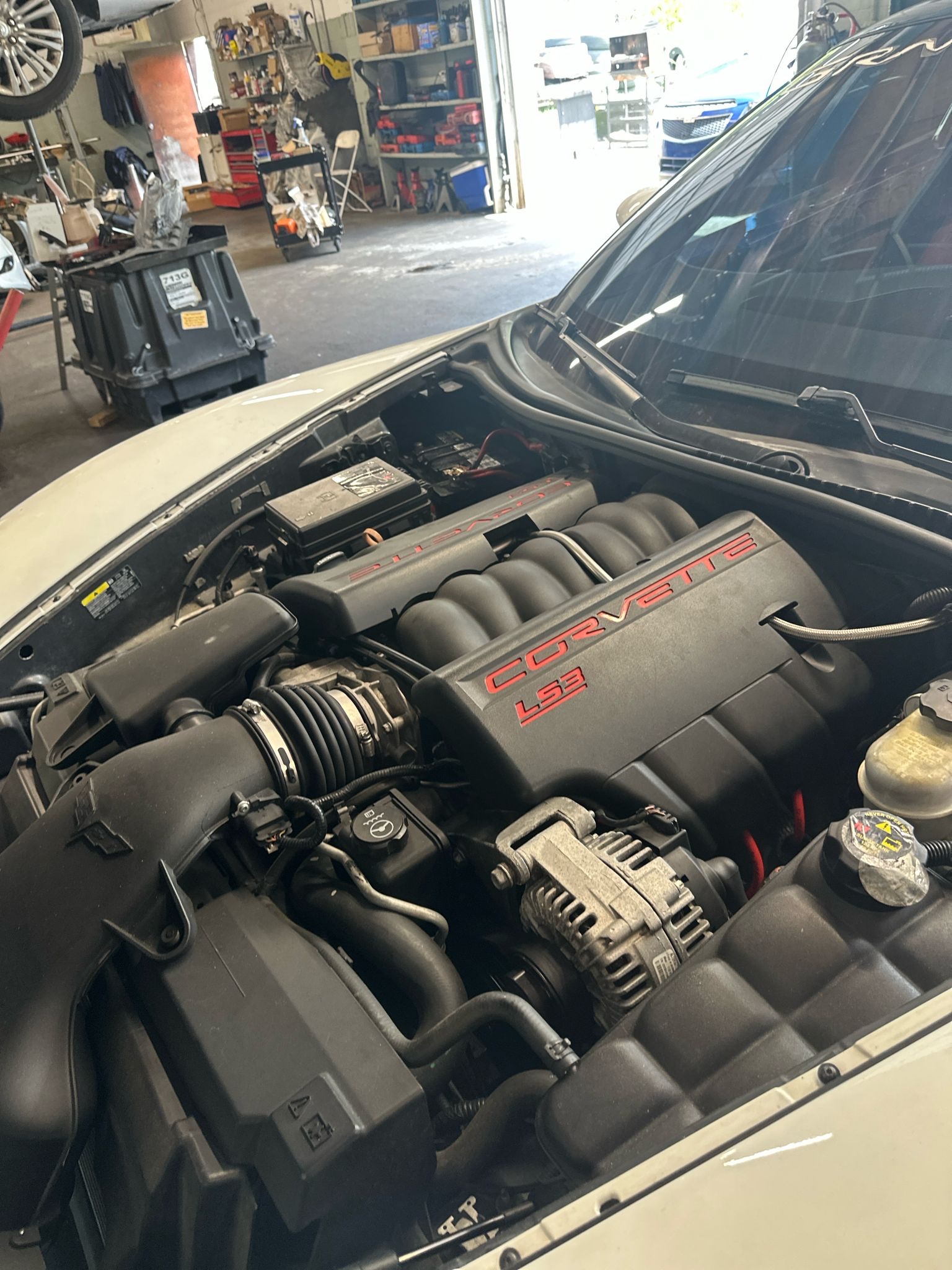 A Corvette LS3 engine bay with the shop shelves behind it